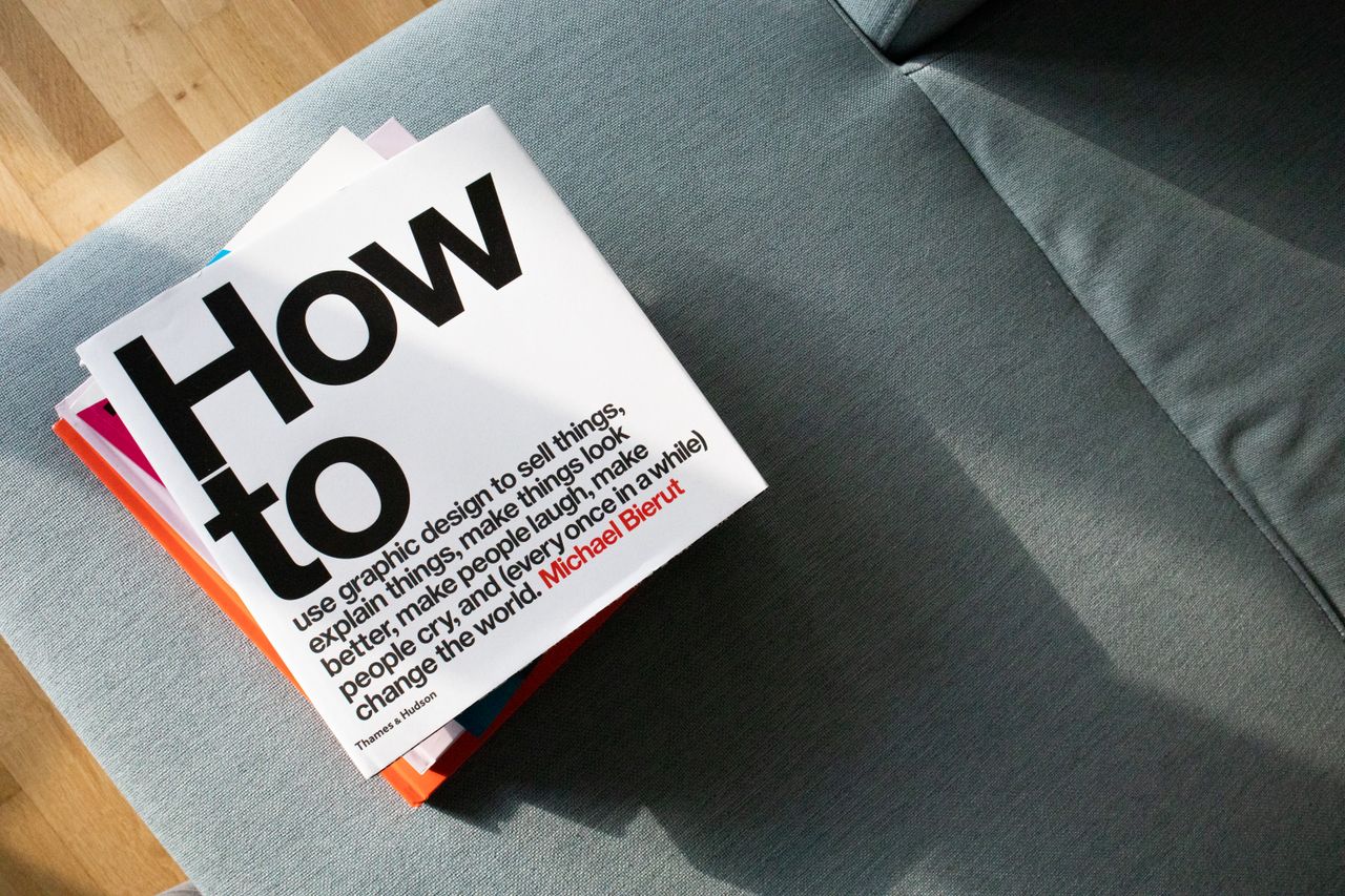 our-story A collection of design books on a couch, showcasing How to by Michael Bierut